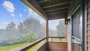 Un balcón de madera con vista a un bosque y un edificio a lo lejos.