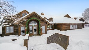 Una cabaña de madera con techo nevado y una entrada acogedora decorada con follaje.