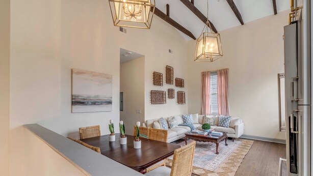 A spacious living room with a dining area, wooden flooring, a large sofa, and a kitchen area with a refrigerator. - The Manor 93 - B Beautiful Three Bed Three Bath Close to King St. (Charleston)