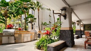 An outdoor patio with a barbecue area, stone seating, and tropical plants.