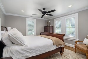 Un dormitorio con cama, cómoda de madera, una silla y ventilador de techo.
