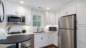 A modern kitchen with white cabinets, stainless steel appliances, a black countertop, and a window with blinds. - View Street Retreat | Pet Friendly, Fenced Yard, Walk to Town! (Black Mountain)