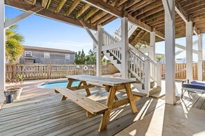 Eine Holzterrasse mit Pool, Picknicktisch und überdachtem Bereich mit Treppe.