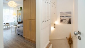 A modern living room with a sofa, a coffee table, and a lamp. There is a wooden cabinet and a white wall with a painting. - Syltoase - 3-zimmer App. für 4 Personen mit Terrasse, Stellplatz, Wlan. Haustier Erlaubt (Westerland)