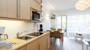 A modern kitchen with wooden cabinets, a built-in oven, and a dining area with a table and chairs. - Syltoase - 3-zimmer App. für 4 Personen mit Terrasse, Stellplatz, Wlan. Haustier Erlaubt (Westerland)
