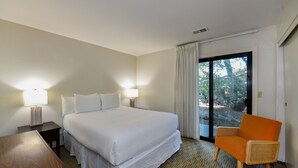 A hotel room with a large bed, two bedside lamps, a wooden nightstand, a wicker armchair, and a sliding glass door leading to an outdoor area. - Private Golf Resort Setting 3 bedrooms (Napa)