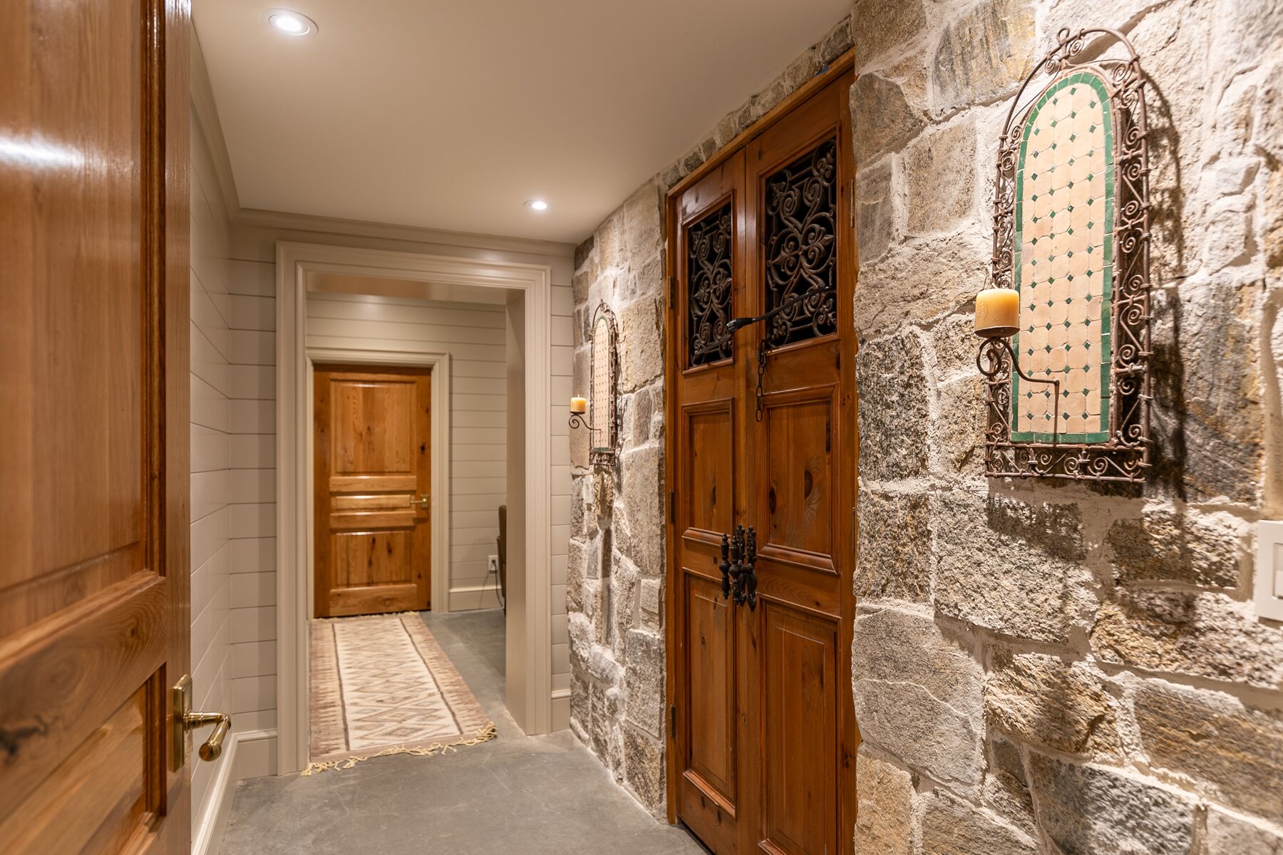 A hallway with stone walls, wooden doors, and a patterned rug.