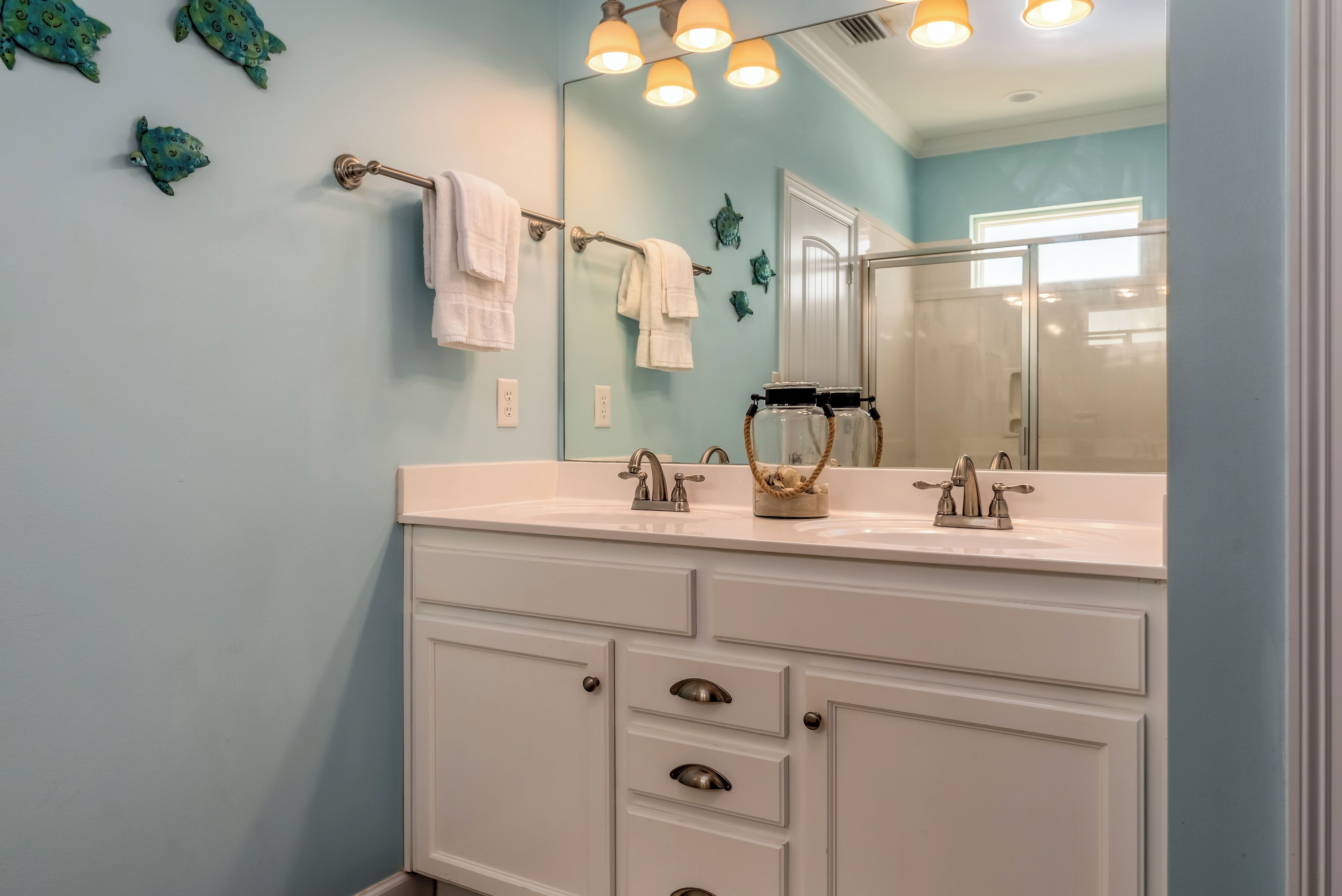 A bathroom with a light blue wall, white vanity with drawers, a mirror, and a towel rack.