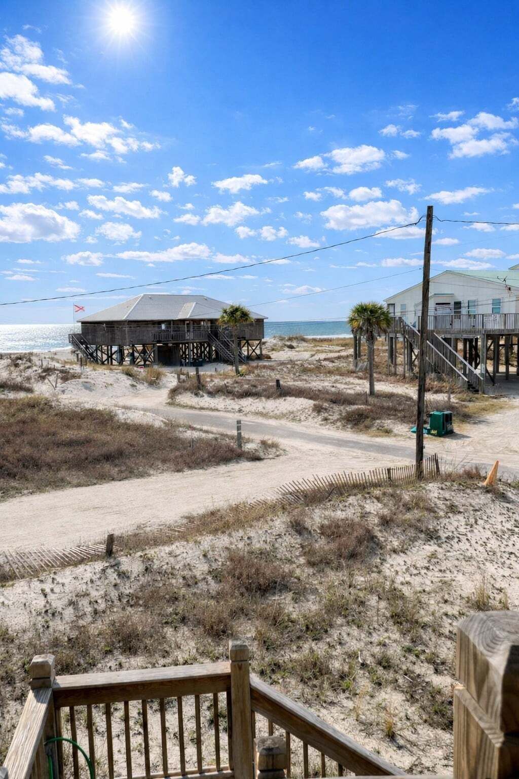 Une maison de plage dotée d’une terrasse en bois, d’un escalier menant à une jetée et offrant une vue sur l’océan.