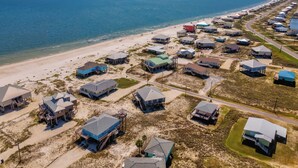 An aerial view of a coastal residential area with houses on stilts, a beach, and a clear view of the ocean. - Tidewater East | Gulf-Side Comfort & Style (Dauphin Island)