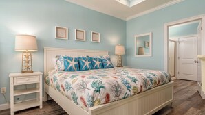A bedroom with a bed, two nightstands, a mirror, and a door. - Tidewater East | Gulf-Side Comfort & Style (Dauphin Island)