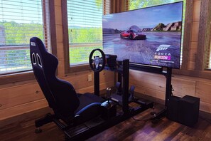 A gaming setup with a racing game on screen, a racing wheel, and a high-end gaming chair. - Sierra Cascades - Indoor Pool, Driving Simulator & Mountain Game Loft (Sevierville)