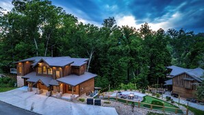 Una cabaña moderna de troncos con base de piedra, un patio con mobiliario exterior y vistas a una zona boscosa.