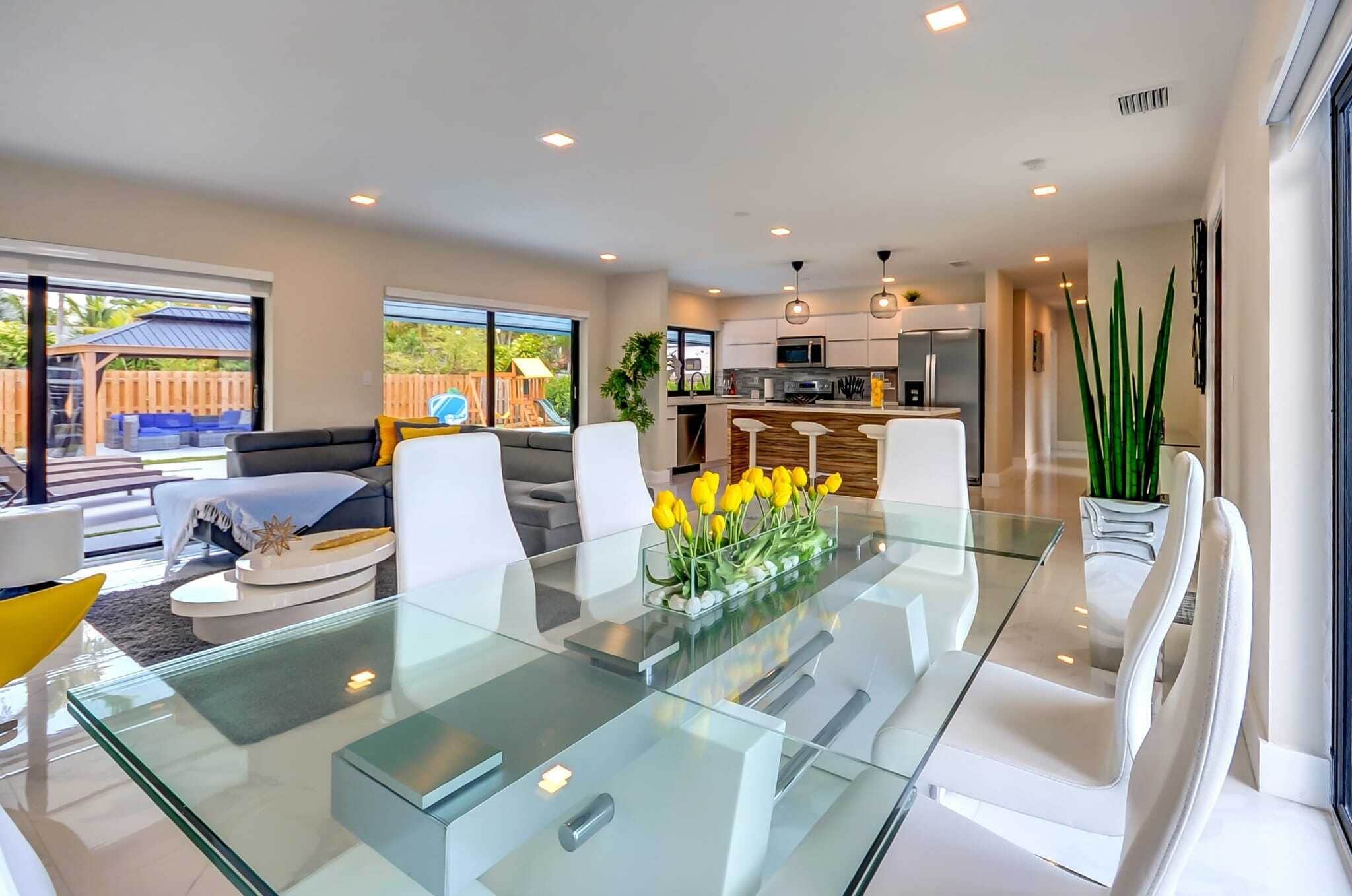 A modern kitchen with white cabinets, a central island, and a dining area with a glass table and white chairs.