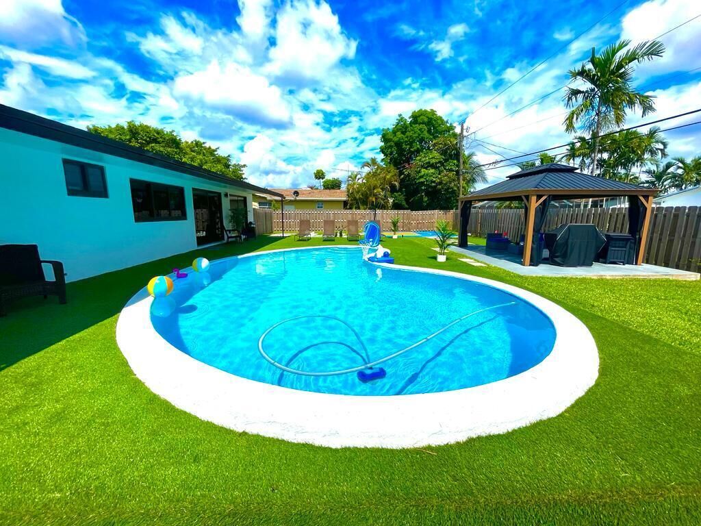 Un jardin avec une piscine, un patio couvert et un espace clos agrémenté de palmiers.