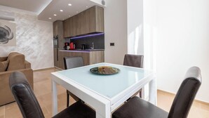 Una sala moderna con una mesa de comedor de vidrio, un sofá y una zona de cocina con armarios de madera e iluminación debajo de los gabinetes.