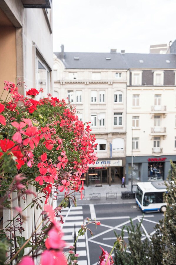 A street view with a row of red flowers in the foreground, buildings in the background, and a bus on the street.