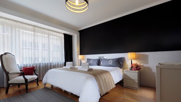 Una habitación de hotel moderna con una cama grande, una silla, una mesita de noche y un escritorio.