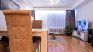 Una sala de estar moderna con una mesa de comedor de madera, un sillón marrón capitonado, un televisor y una araña.