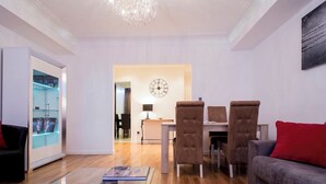 Una sala de estar moderna con una mesa de centro de vidrio, un sofá con un cojín rojo y una zona de comedor con un reloj en la pared.