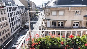 A city street with buildings, a tram, and a balcony with flowers.
