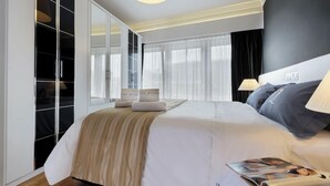 A modern hotel room with a large bed, a wardrobe, and a window with sheer curtains.