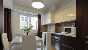 Una cucina moderna con mobili bianchi, un forno a microonde e un'area pranzo con un tavolo in vetro e sedie.