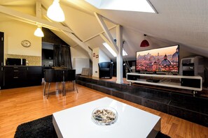 Una sala de estar moderna con televisor de pantalla plana, un comedor con sillas y una cocina al fondo.