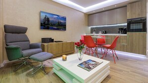 A modern living room with a sofa, a coffee table, and a dining area with red chairs.