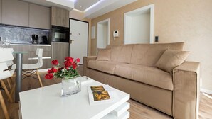 A modern living room with a beige sofa, a glass coffee table with a vase of red flowers, and a white dining table.