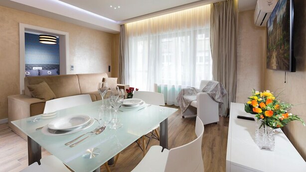 A modern dining area with a glass table set for four, a sofa, and a TV mounted on the wall.