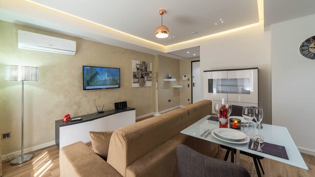 Ein modernes Wohnzimmer mit einer Couch, einem Esstisch gedeckt mit Tellern und Gläsern, einem flachbildfernseher an der Wand und einer Deckenleuchte.
