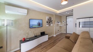 Ein modernes Wohnzimmer mit Flachbildfernseher, einer weißen Unterhaltungsecke, einem braunen Sofa und einer Stehlampe.