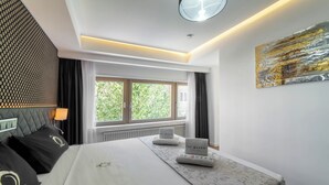 Ein Hotelzimmer mit einem großen Bett, einem Fenster mit Vorhängen, einem Wandbild und einer Deckenleuchte.