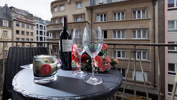 Una mesa con una botella de vino, dos copas de vino y una vela en un balcón con vista a edificios de apartamentos.