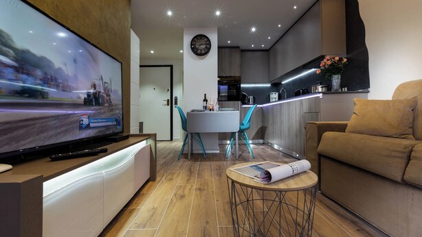 A modern living room with a flat-screen TV, a dining table with chairs, a sofa, and a small round table with a magazine.