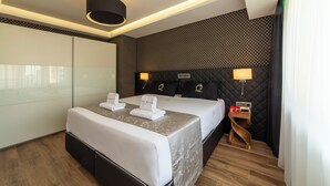 Habitación de hotel con dos camas, diseño moderno y una pequeña mesita de madera con lámpara.