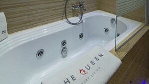 Une salle de bain moderne avec une grande baignoire portant l’inscription « THE QUEEN LUXURY LIVING », une douche à parois de verre et des panneaux muraux en bois.