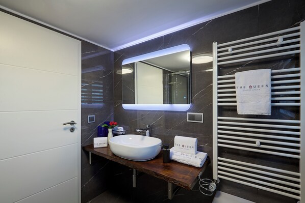 A modern bathroom with a white sink, a mirror, and a towel rack with a towel labeled "The Queen."