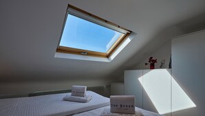 Un dormitorio con dos camas, un tragaluz y un armario blanco.