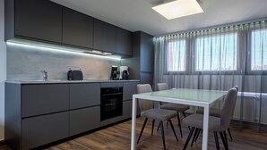 Una cocina moderna con electrodomésticos integrados, un comedor con mesa y sillas de vidrio, y ventanas amplias con cortinas translúcidas.