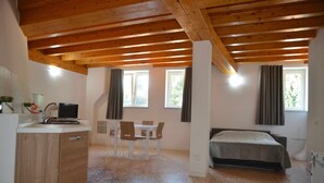 A bedroom with a bed, a desk, and a chair. There is a window with curtains, a wooden ceiling, and a carpeted floor. - Palazzo Maggiore Suite A (Noale)