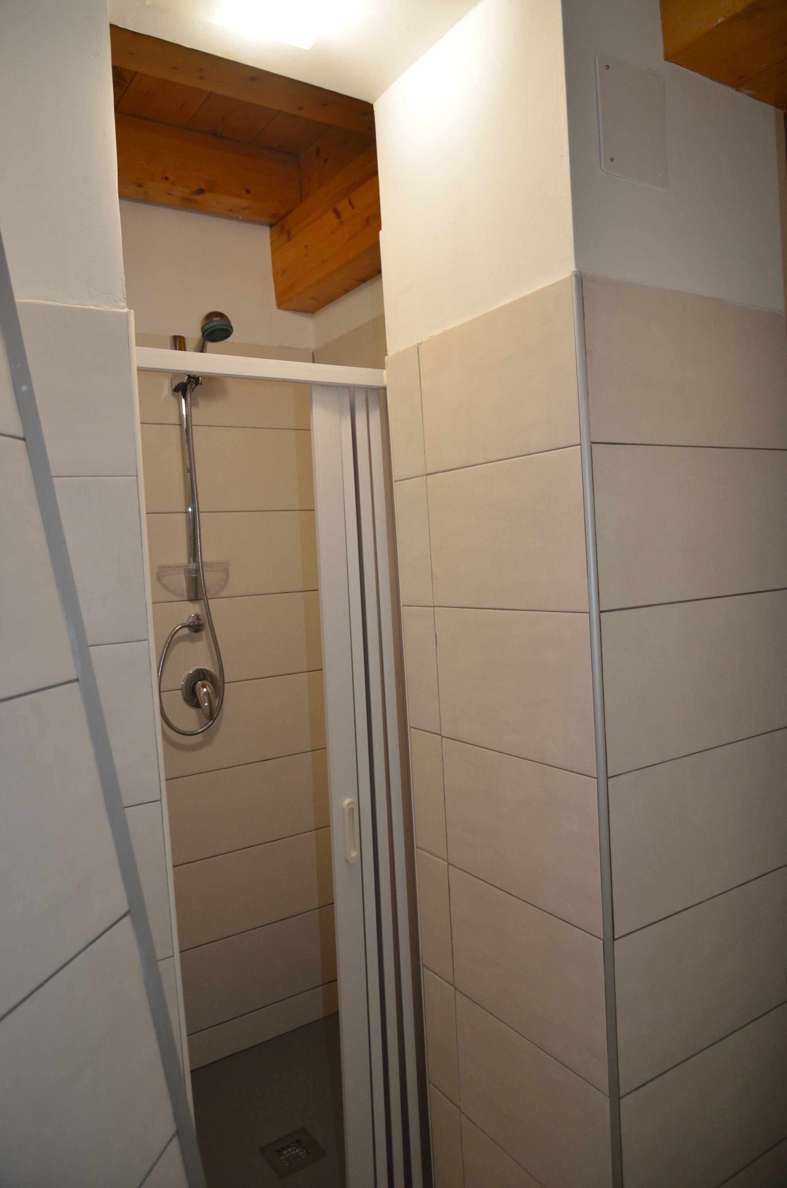Een kleine, afgesloten douchecabine met betegelde wanden en een houten plafond.