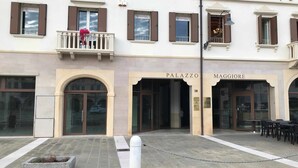 A building with 'PALAZZO' and 'MAGGIORE' entrances, a small balcony with flowers, and a chain-locked bollard in the foreground. - Palazzo Maggiore Suite A (Noale)