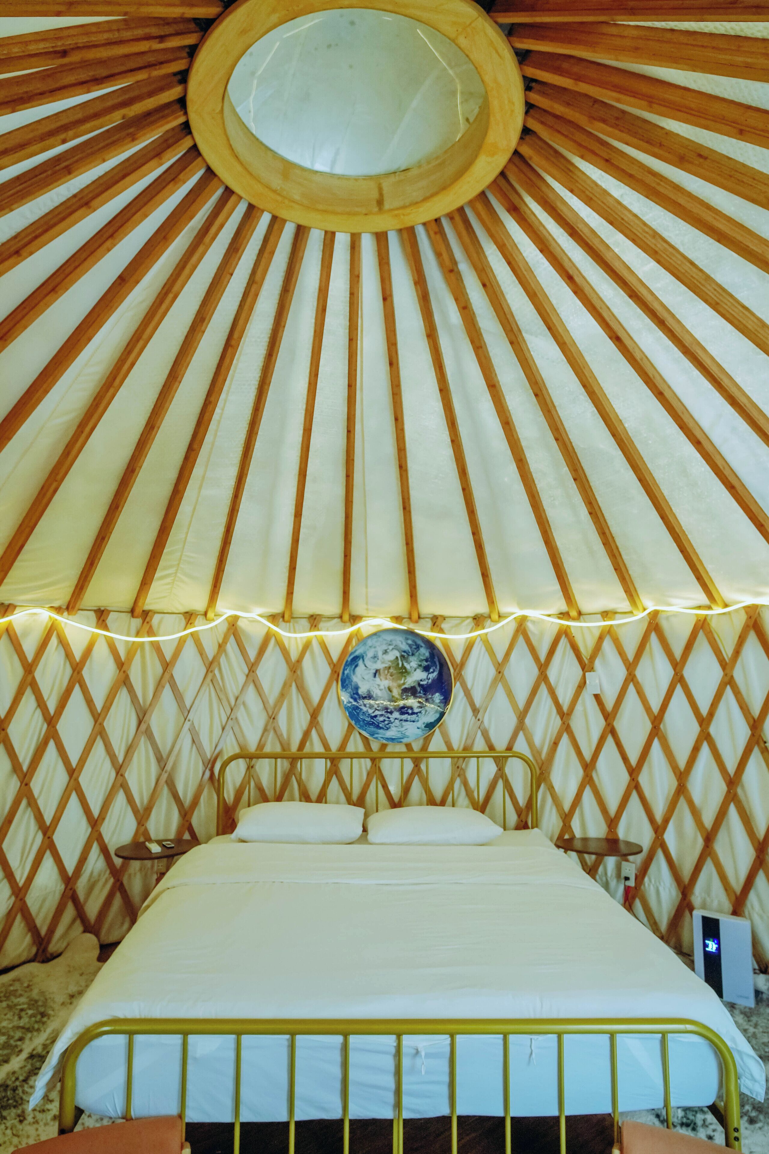 A traditional yurt interior with a bed, wooden lattice walls, and a circular skylight.