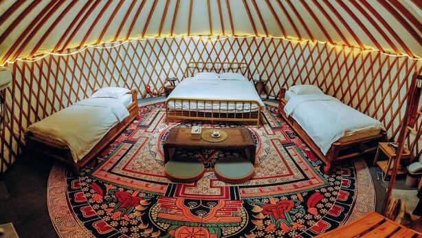 A yurt with a central bed, two side beds, and a patterned floor. - Nomad Yurts (Coron)