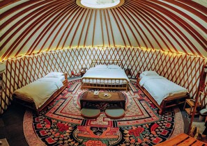 A yurt with a central bed, two side beds, and a patterned floor. - Nomad Yurts (Coron)