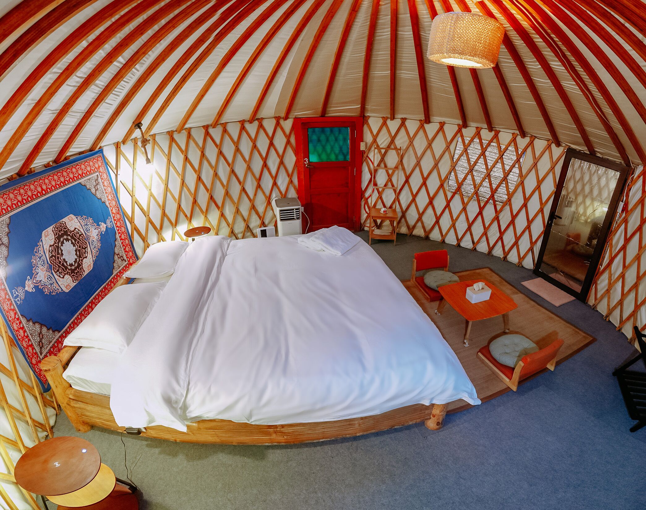 Una yurta con cama, una mesita, una silla y una lámpara colgante.