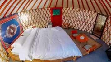 Una yurta con cama, una mesita, una silla y una lámpara colgante.