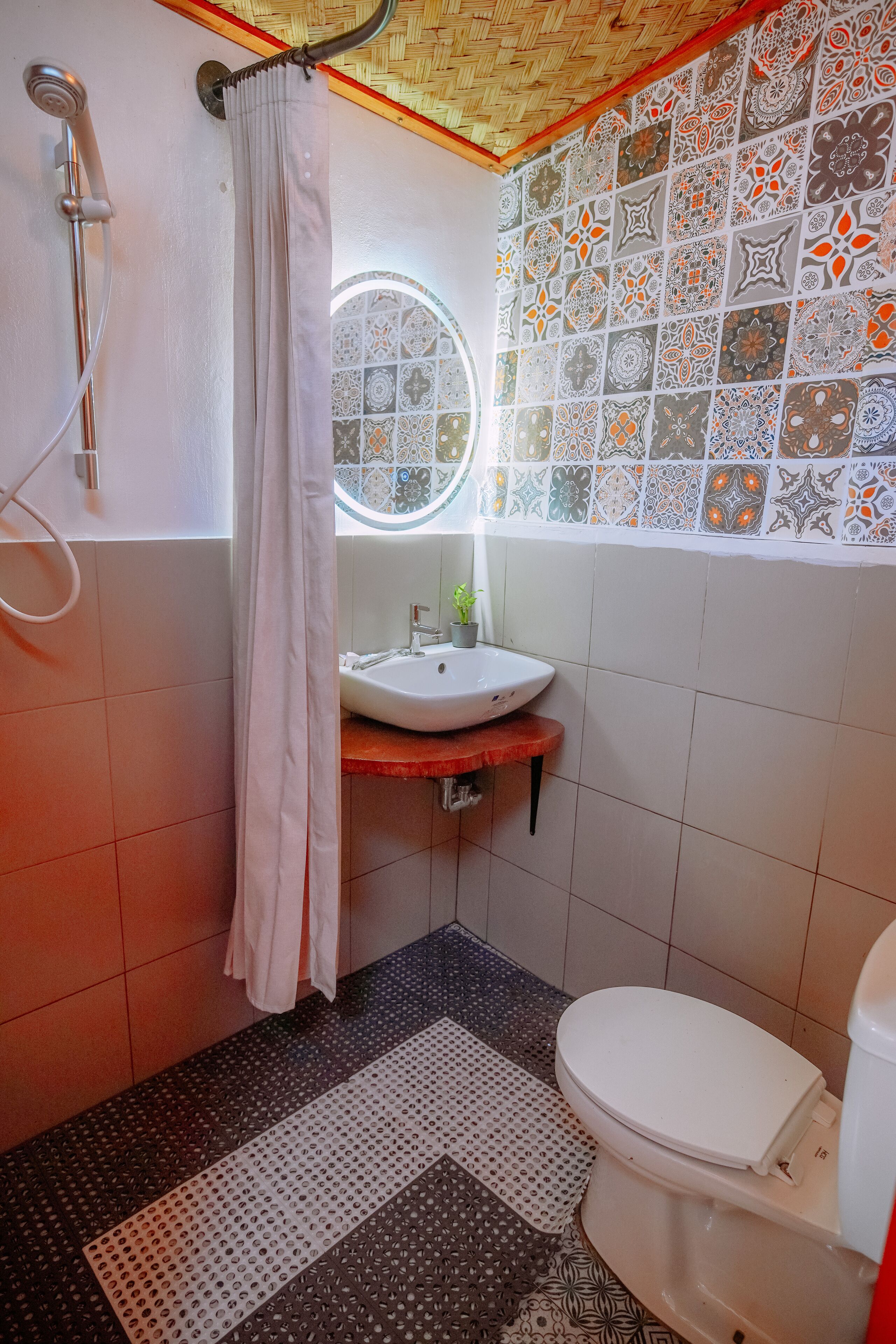 Een badkamer met douche, toilet, wastafel en decoratieve tegels.